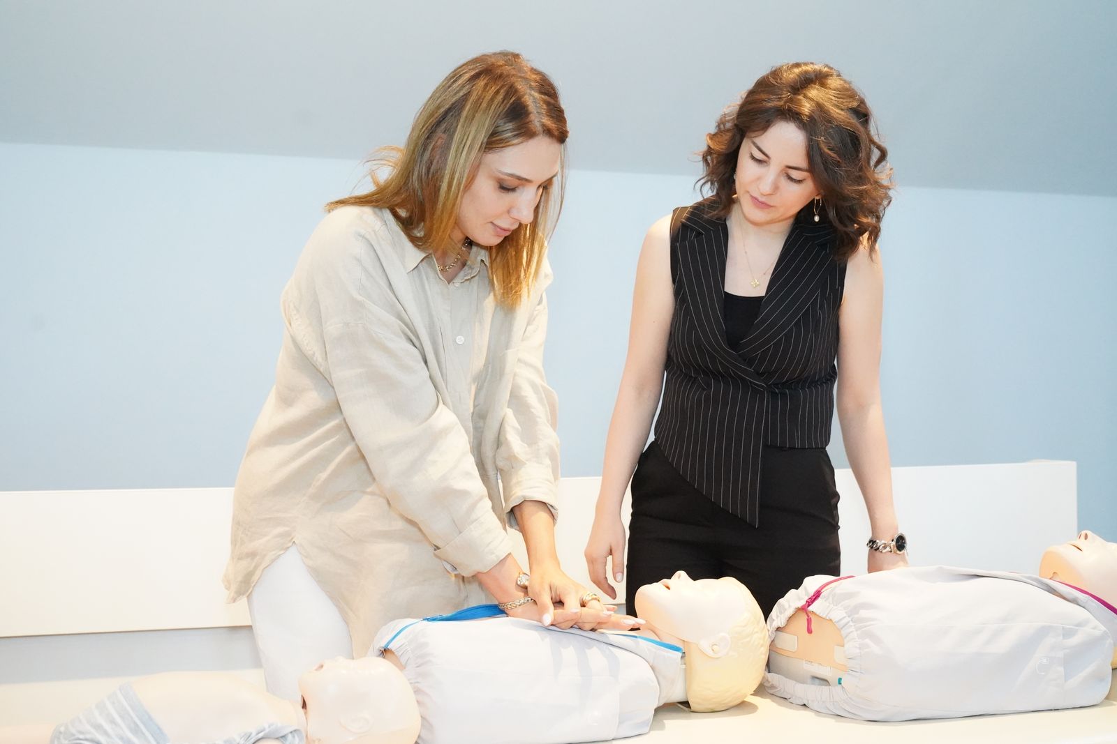 Trainerin zeigt einer Teilnehmerin im Präsenztag des Hybrid-Kurses die Herzdruckmassage an der Trainingspuppe