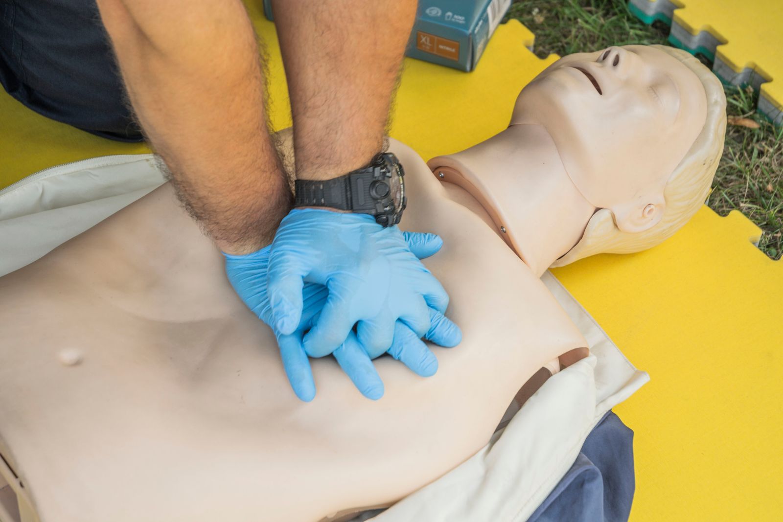 Nahaufnahme: Herzdruckmassage mit Handschuhen an einer Trainingspuppe während der 8h Auffrischung